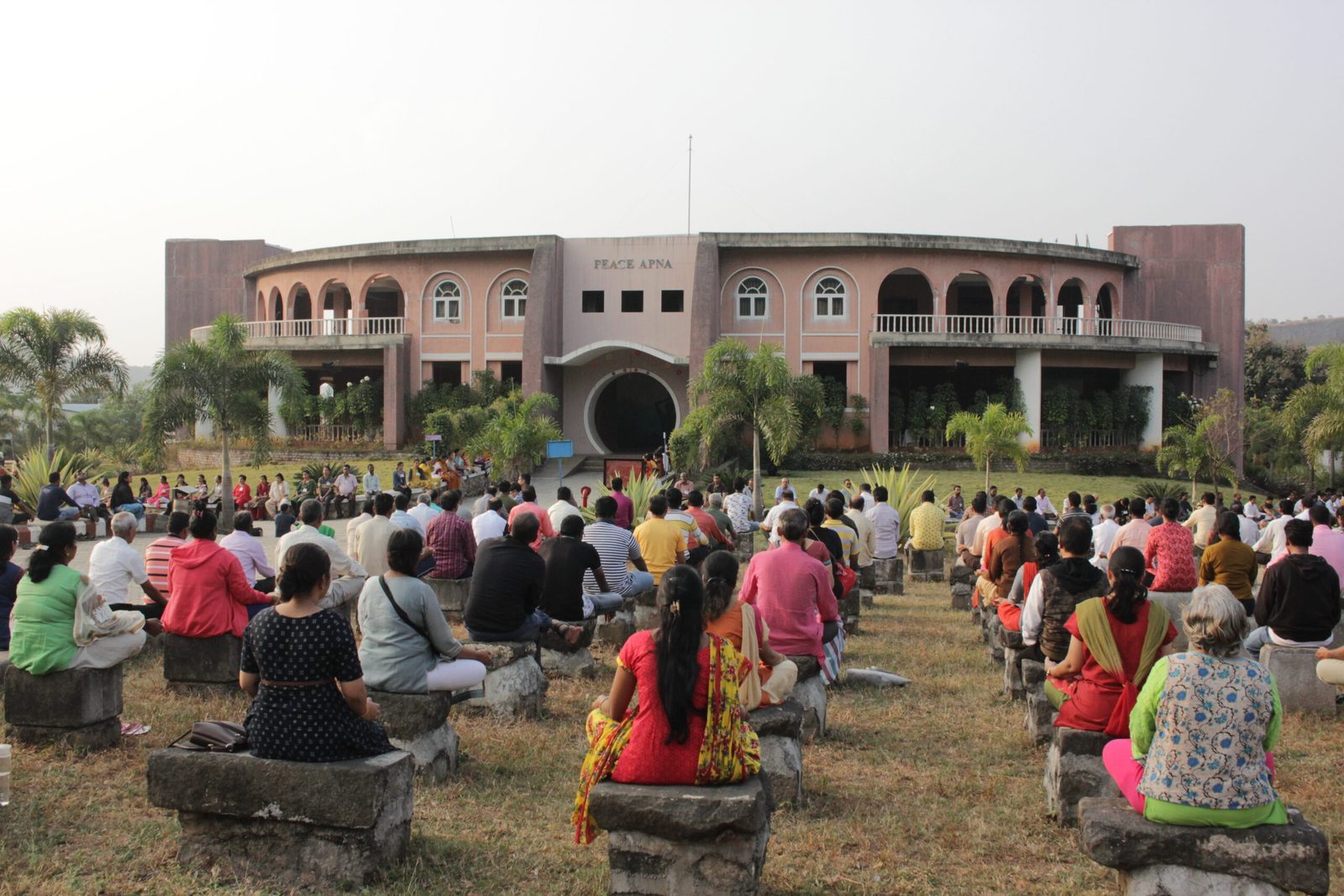 Seekers meditating on the lawn facing the Peace Apna building at dawn